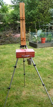 a red box sitting on top of a tripod in the middle of a yard