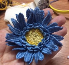 a hand holding a blue and yellow flower on top of a wooden table next to yarn