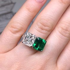 an emerald and diamond ring on someone's finger, with the engagement ring setting in white gold