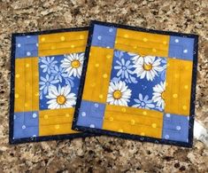 two yellow and blue coasters with white daisies on them sitting on a granite countertop