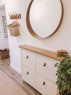 a white dresser sitting next to a mirror and potted plant on top of it