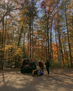 two people standing next to a car in the woods