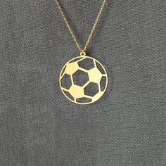 a gold necklace with a soccer ball cut out in the middle on a gray background