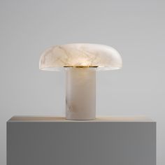 a white table lamp sitting on top of a wooden block next to a gray wall