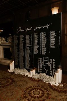 a table with candles and seating chart on the wall in front of an area rug