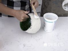 a person using a brush to paint the inside of a vase with white glaze