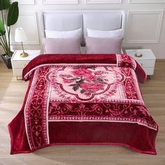 a bed covered in a red and white comforter next to two pillows on top of a wooden floor