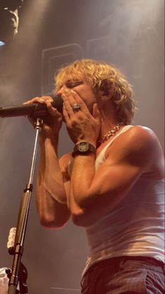 a man holding his face to his mouth while standing in front of a microphone on stage