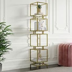 a gold metal shelf with books and plants on it next to a pink velvet chair