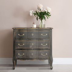 an old dresser with flowers and candles on it in front of a pink painted wall