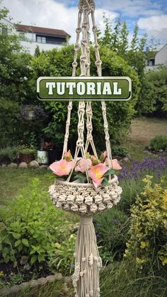 a bird feeder with flowers hanging from it's sides in front of some bushes