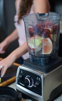 a blender filled with fruit sitting on top of a counter next to a cutting board