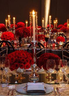 the table is set with red roses, candles and silverware for an elegant dinner