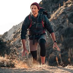 a man with a backpack is hiking up a hill in the mountains and has his hands out