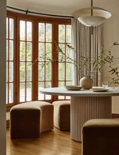 a dining room table with chairs and vases on it in front of large windows