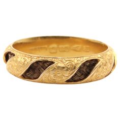 A gold and hairwork ring, comprising plaited hair within a chased band of 18 karat yellow gold. This beautiful ring is adorned with beautiful floral and foliate chasing around the band. Openwork panels are evenly spaced around the band, revealing the plaited brunette hairwork within the band. The wide, domed band is the same width all the way around the ring. The ring is in excellent condition and the hairwork is in great condition. The. Wear and tear acquiescent with age. The band measures 6mm wide. Gross weight: 3.12g Ring size: due to the width of this ring, it fits like a UK – P US – 7.75 EU – 56.25 mm (actual size UK – R.5 US – 9 EU – 59.5 mm) Hallmarks: 18 (18 karat gold), Chester, date letter ‘E’ for 1823, bearing a rubbed makers mark that looks to be "WGM Byzantine Yellow Gold Engraved Rings, Victorian Yellow Gold Carved Rings, Antique Baroque Yellow Gold Jewelry, Ancient Style Collectible Yellow Gold Rings, Plaited Hair, Collectible Art Nouveau Yellow Gold Ring, Plaits Hairstyles, Beautiful Ring, Chester