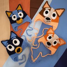 three crocheted animal hats with eyes and ears on top of a blue blanket