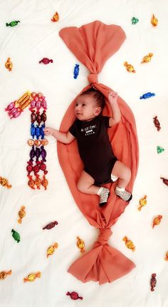 a baby laying on top of a blanket covered in candy candies and wearing a black shirt