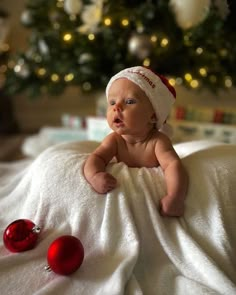 a baby laying on top of a bed next to a christmas tree