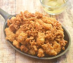 fried food in a frying pan next to a glass of tea