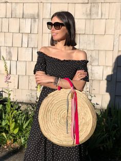 a woman in a black and white dress holding a straw bag with a red ribbon