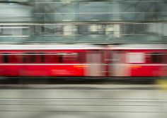 a red and white train traveling past a tall building with lots of windows on it's side