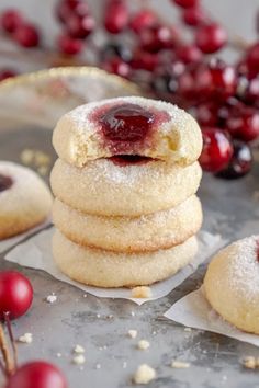 a stack of cookies covered in powdered sugar with cherries on the table next to it