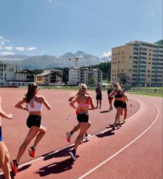 several women running on a track with buildings in the backgrouds and mountains in the background