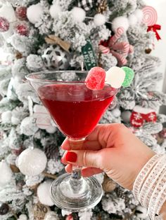 a hand holding a wine glass with red liquid in front of a decorated christmas tree