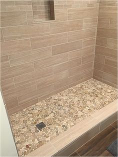 a walk in shower sitting next to a wooden floor and tiled back splash with pebbles on it