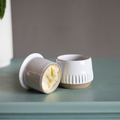 two white cups sitting on top of a green table next to a potted plant