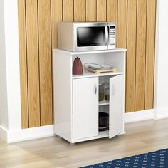 a microwave oven sitting on top of a white cabinet next to a blue rug and wooden wall