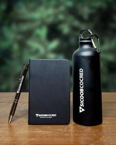 a black water bottle next to a notepad and pen on top of a wooden table