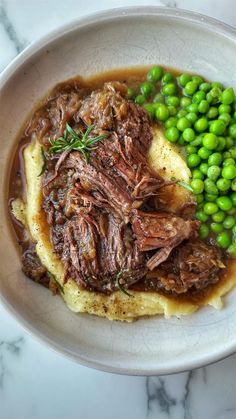 a white bowl filled with meat, mashed potatoes and green peas on top of a marble table