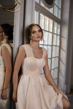 a woman in a white dress leaning against a wall