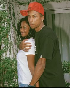 a man and woman standing next to each other in front of a house with ivy growing on the walls