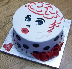 a white cake with red and black designs on it's face, sitting on top of a wooden table