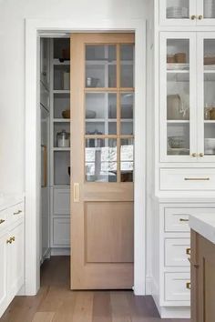 a kitchen with white cabinets and wooden floors, along with an open door leading to the dining room