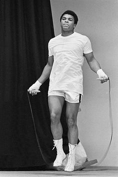 a man in white shirt and shorts holding a tennis racquet next to a black curtain