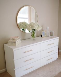 a white dresser with flowers and a round mirror