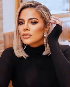 a woman with blonde hair and black top sitting in front of a brick wall wearing large earrings