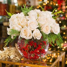 a vase filled with white roses on top of a table next to a christmas tree