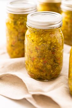 several jars filled with pickles sitting on top of a white cloth covered tablecloth