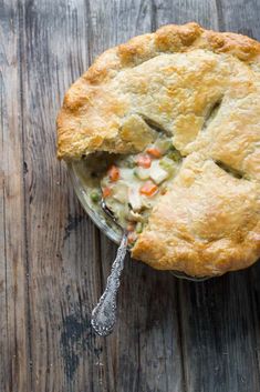 a chicken pot pie with a spoon in it on a wooden table, ready to be eaten