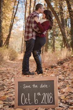 a man and woman kissing in the woods next to a sign that says save the date