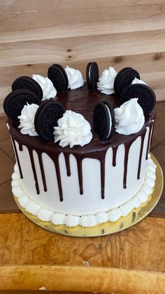 a chocolate cake with white frosting and oreo cookies on top, sitting on a wooden table