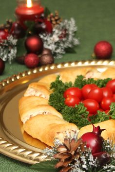 a plate topped with croissants covered in tomatoes and other holiday decorations next to a candle