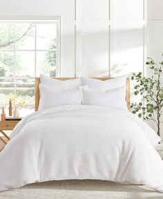 a bed with white comforters and pillows in a room next to a potted plant