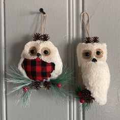 two knitted owls hanging from hooks on a door with pine cones and evergreen needles