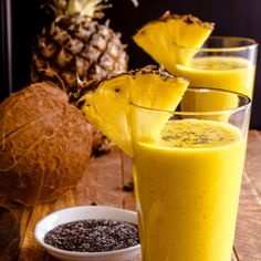 three glasses filled with pineapple smoothie on top of a wooden table next to some fruit